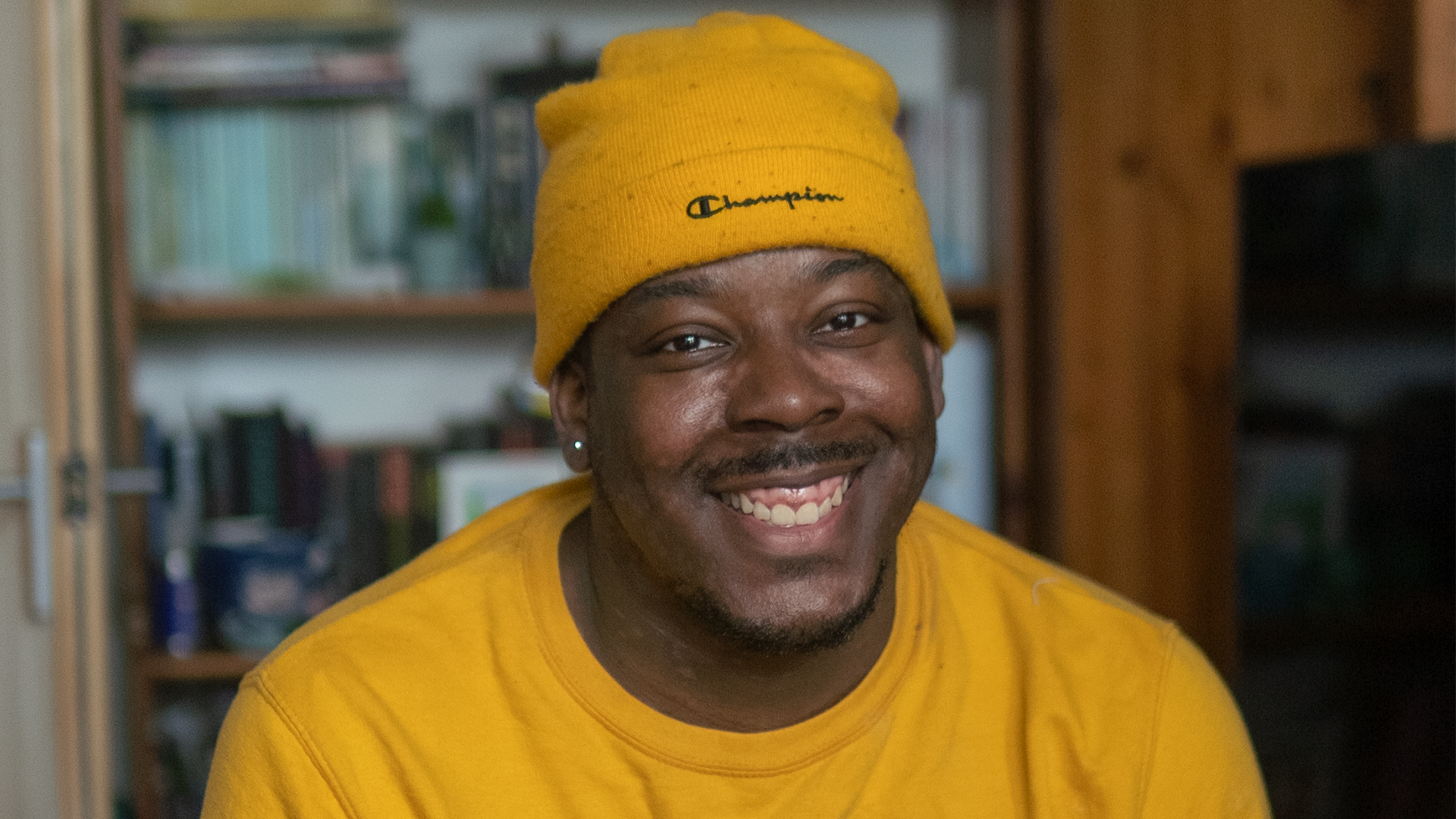A picture of Femi wearing a yellow hat and yellow top and smiling at the camera.
