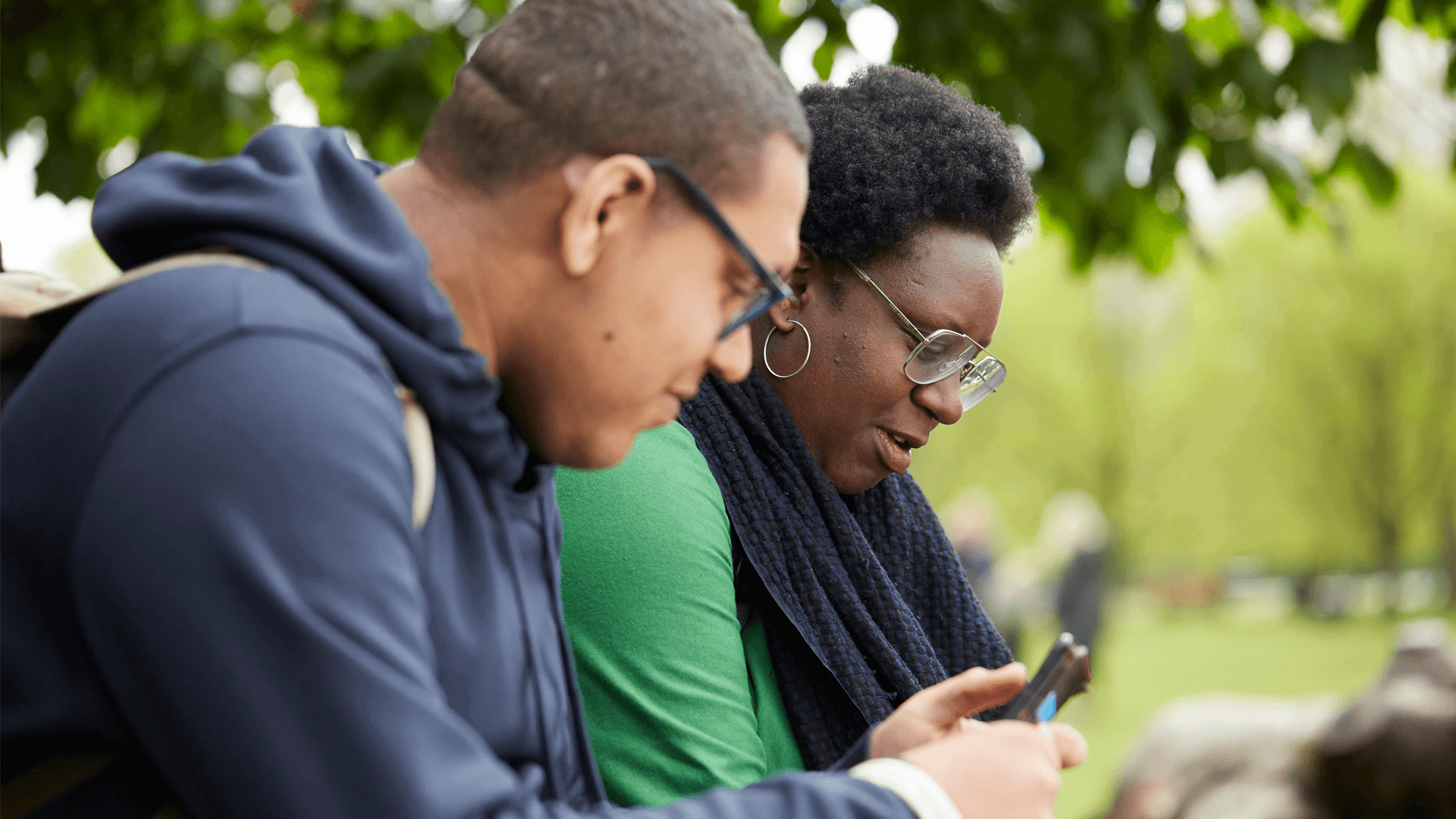 Two people sitting in a park using their mobile phones