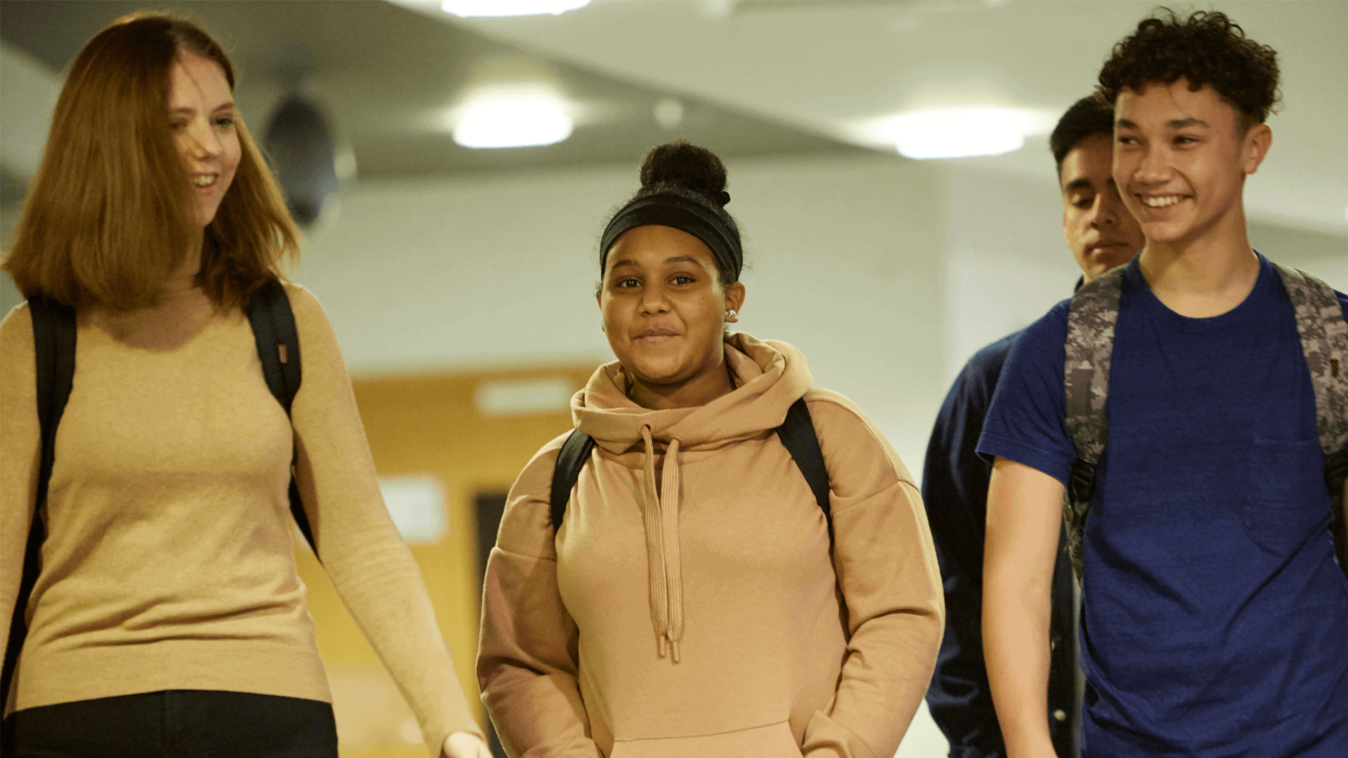 medium shot of four students wearing backpacks smiling while walking in the school hallway