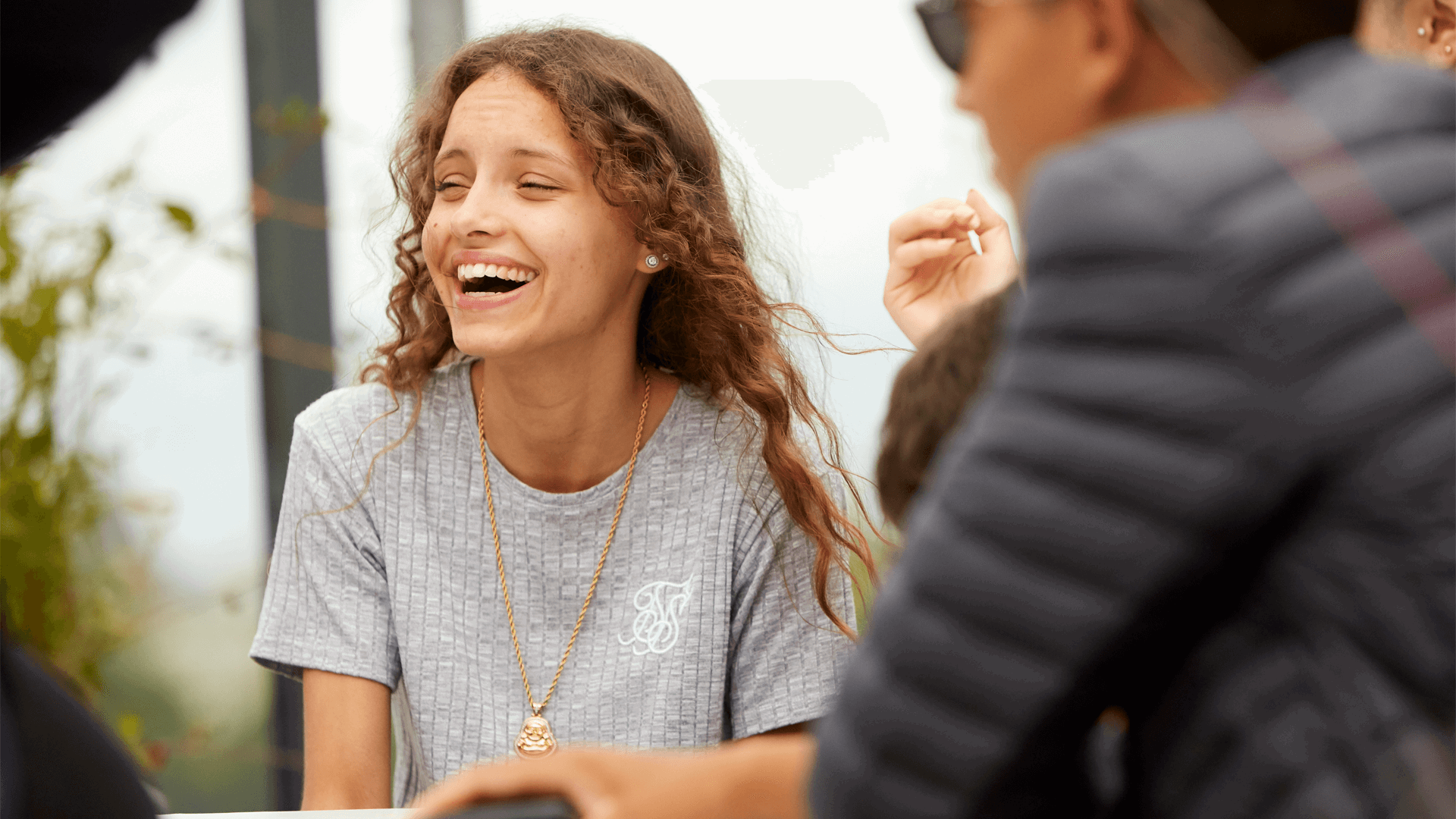 medium-shot-of-a-young-woman-with-curly-hair-wearing-grey-shirt-laughing-while-her-friends-are-around-her