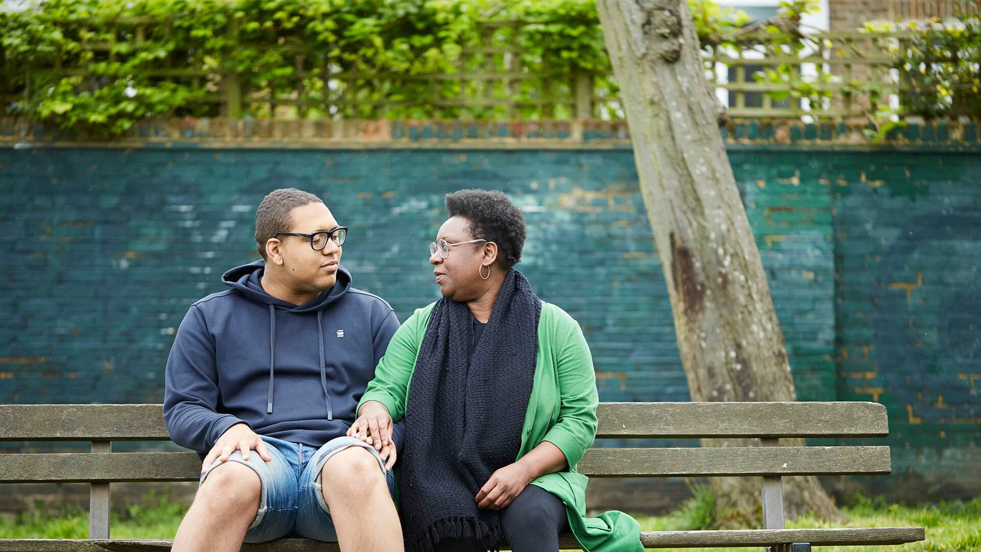 A mother and son holding hands on a bench looking at each other