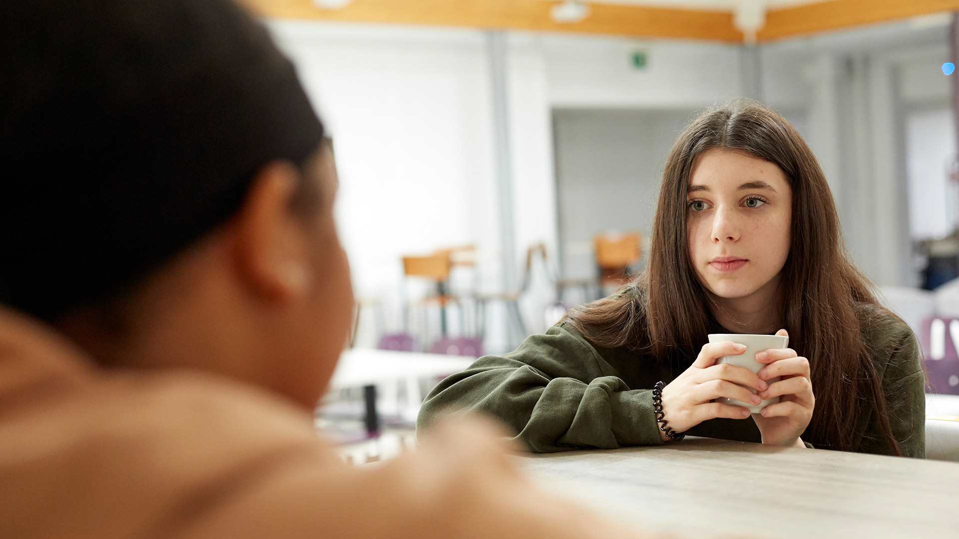 a-girl-holding-a-cup-looking--anxious-while-talking-to-another-person-on-foreground