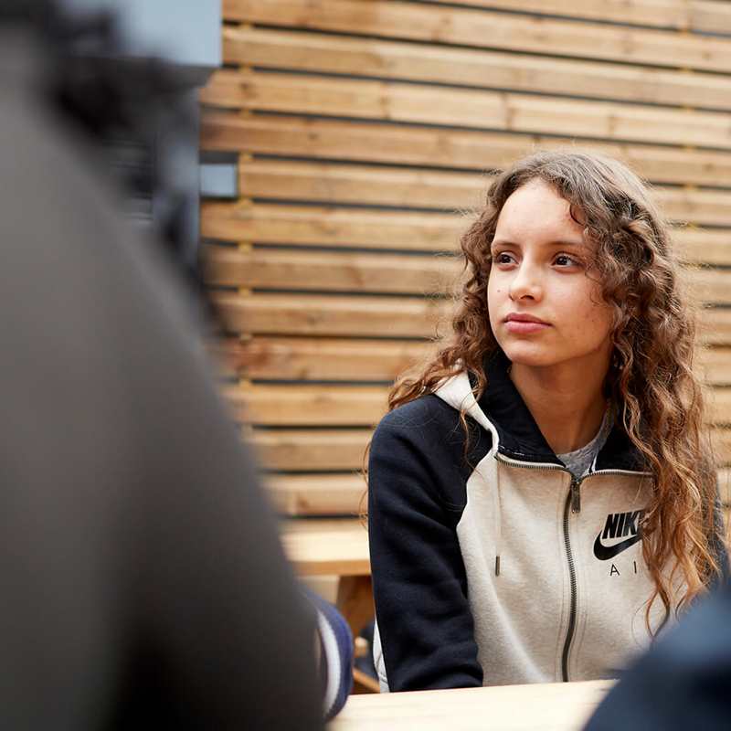 medium-shot-of-a-girl-with-curly-hair-looking-away-while-sitting-in-a-dining-bench-with-friends-around-her