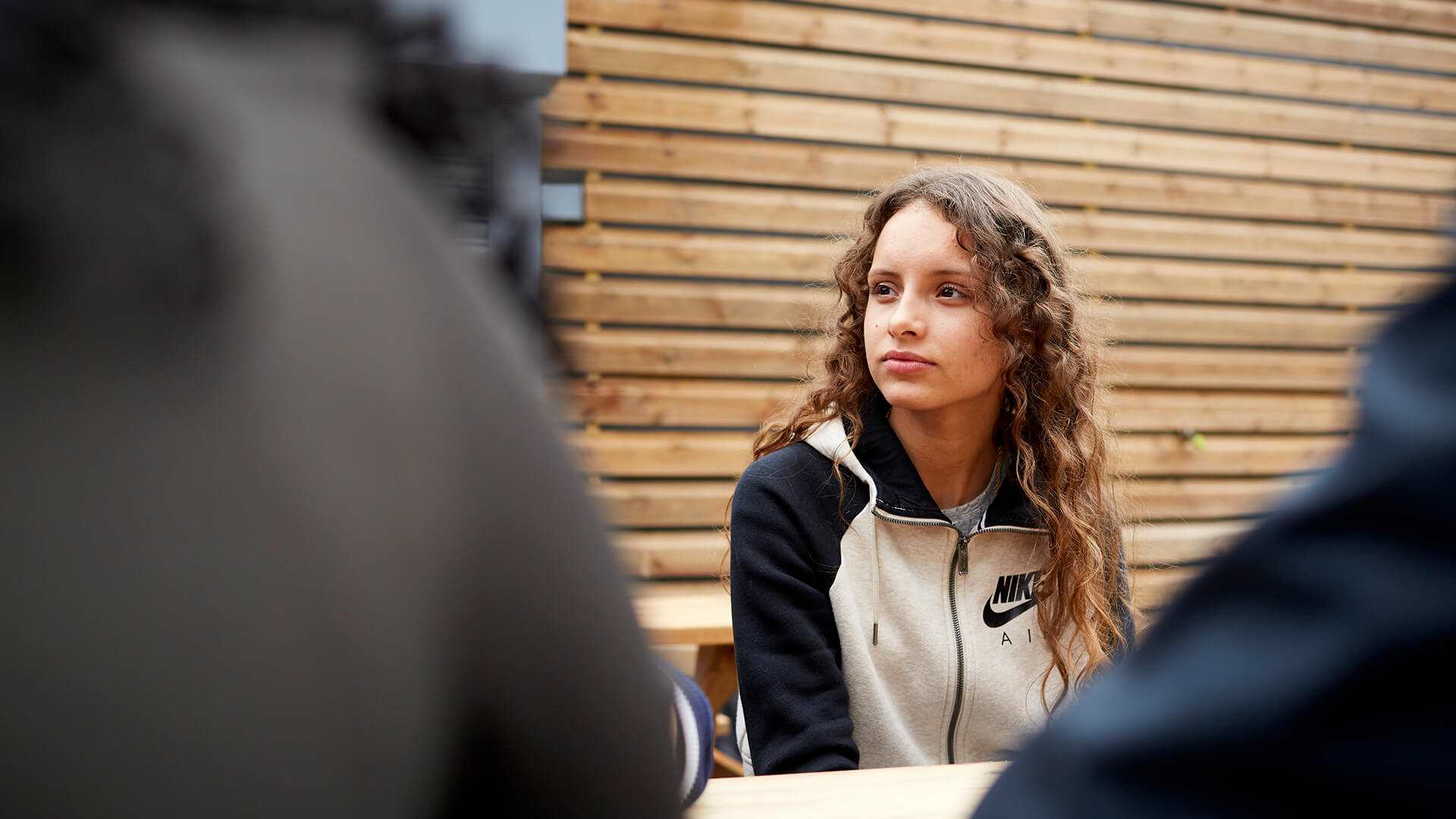 medium-shot-of-a-girl-with-curly-hair-looking-away-while-sitting-in-a-dining-bench-with-friends-around-her