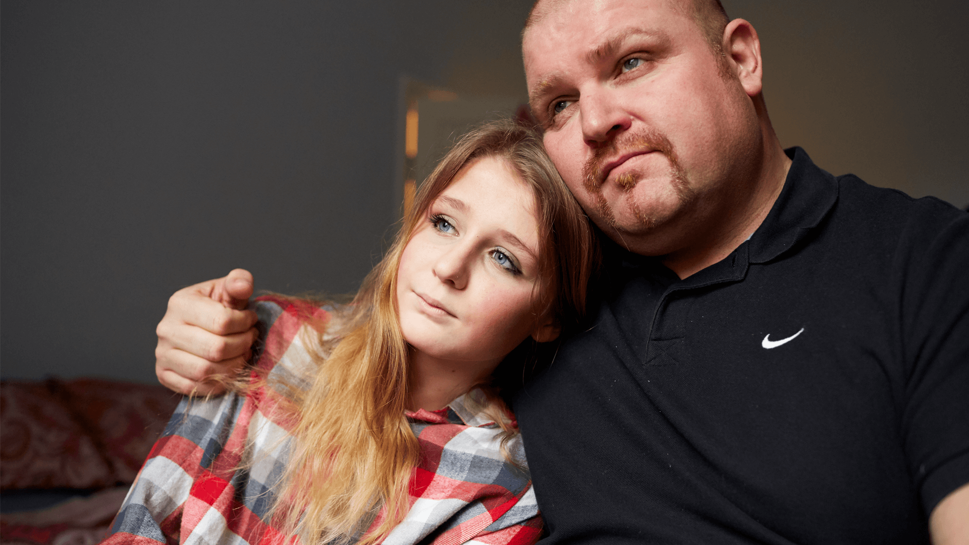 A father with his arm around his young daughter indoors