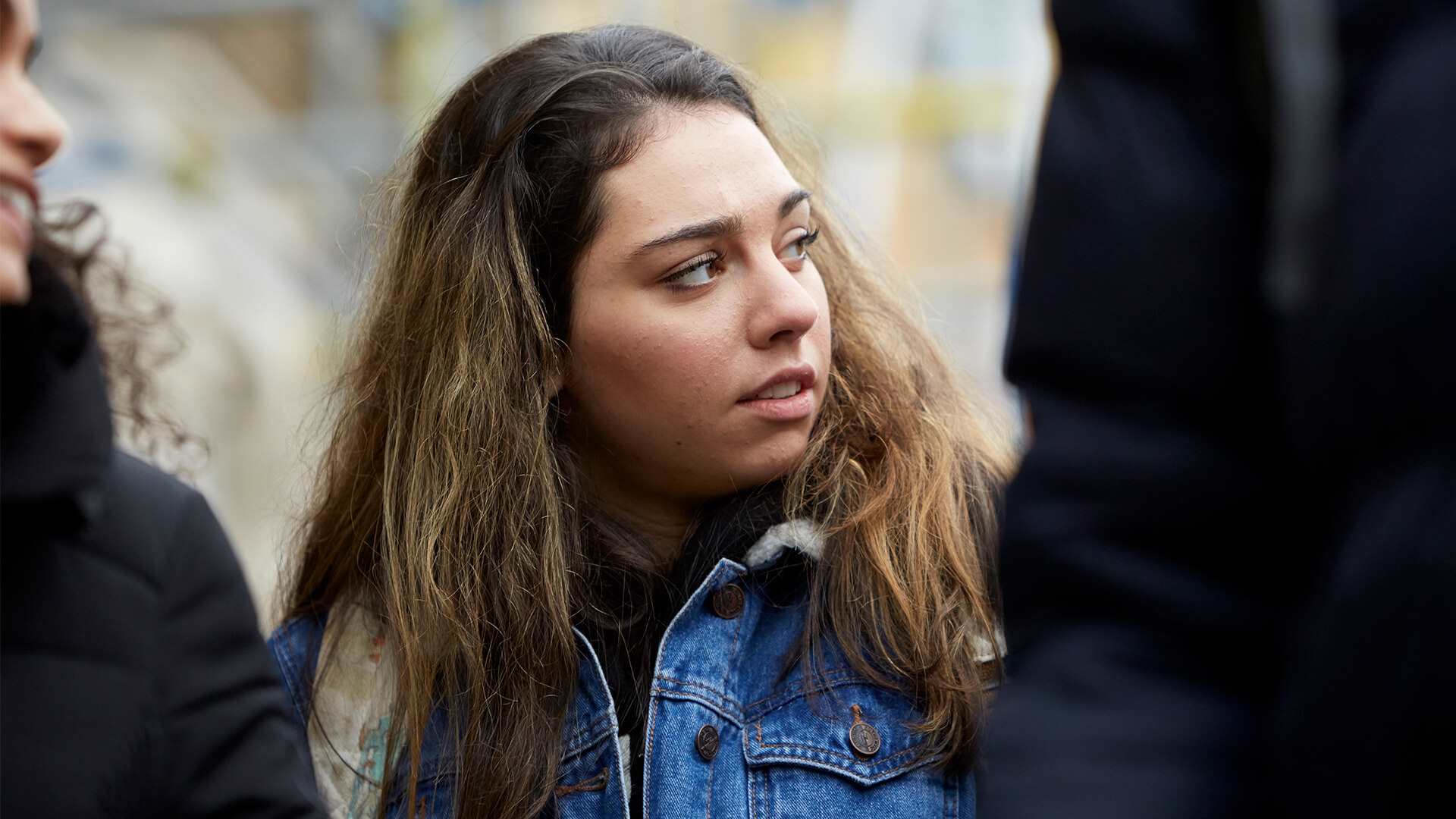 close-up-of-a-young-woman-wearing-blue-denim-jacket-looking-away-while-she-is-in-between-two-other-young-people