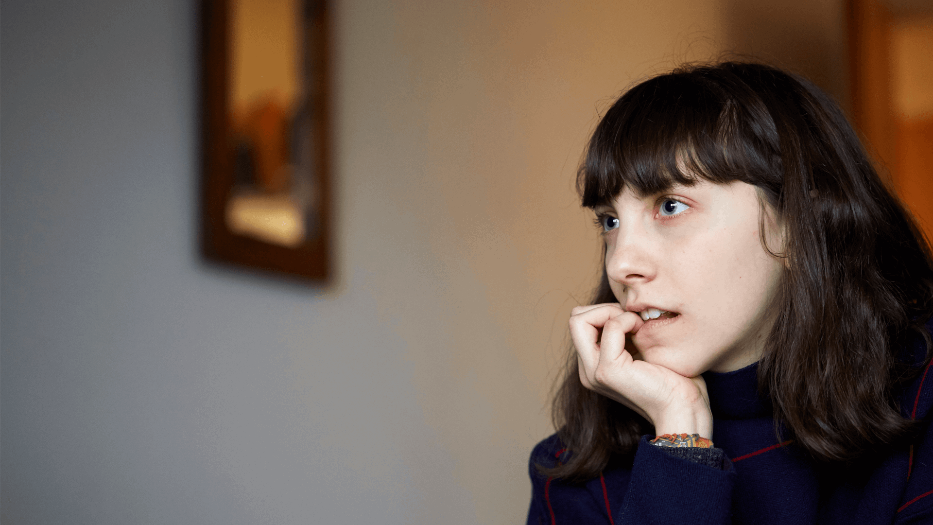 close up of a girl with fringe and wearing black jumper looking away and biting her fingers