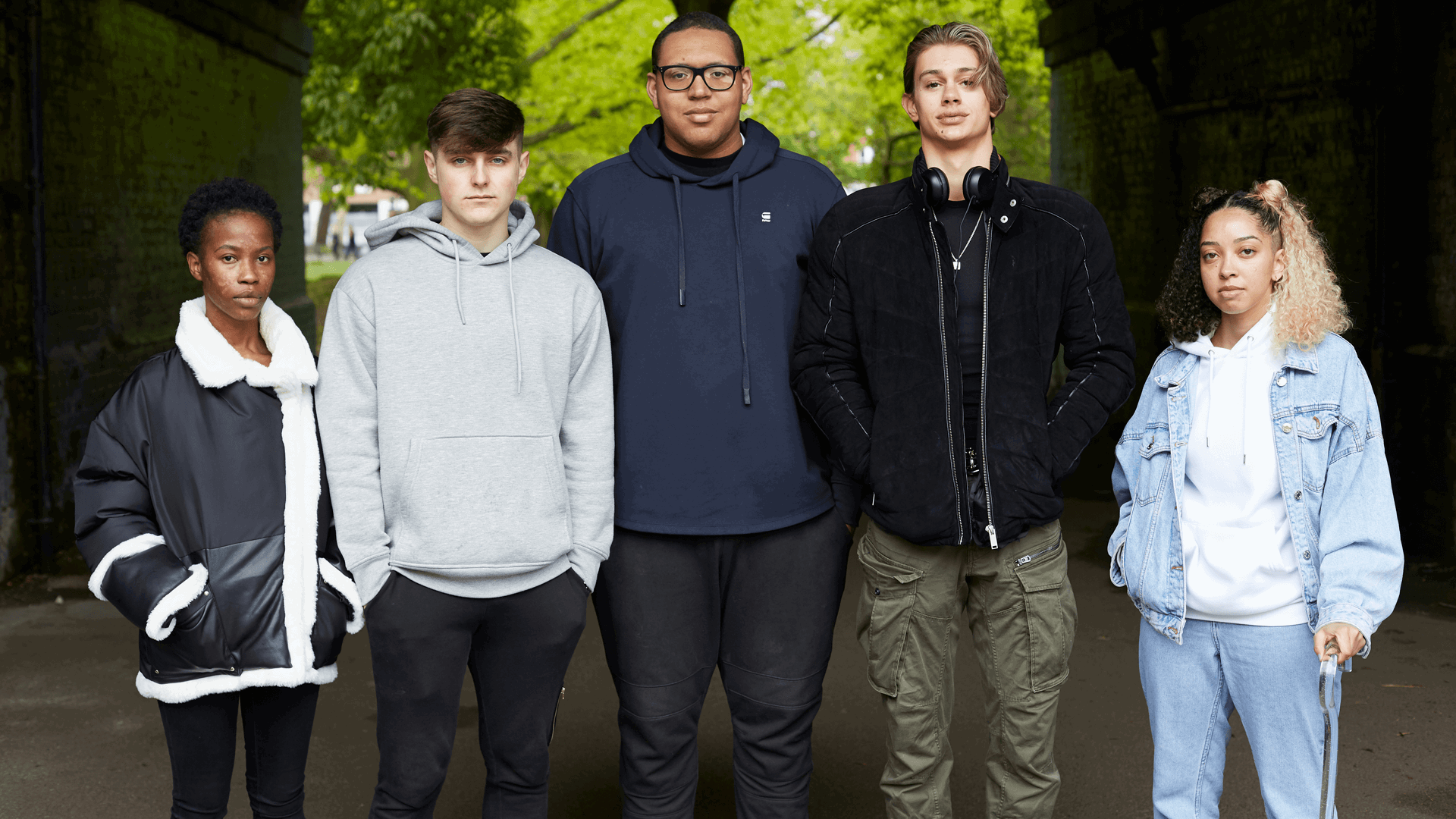 wide-shot-of-a-five-young-people-standing-and-looking-in-front-of-the-camera-with-trees-on-the-background