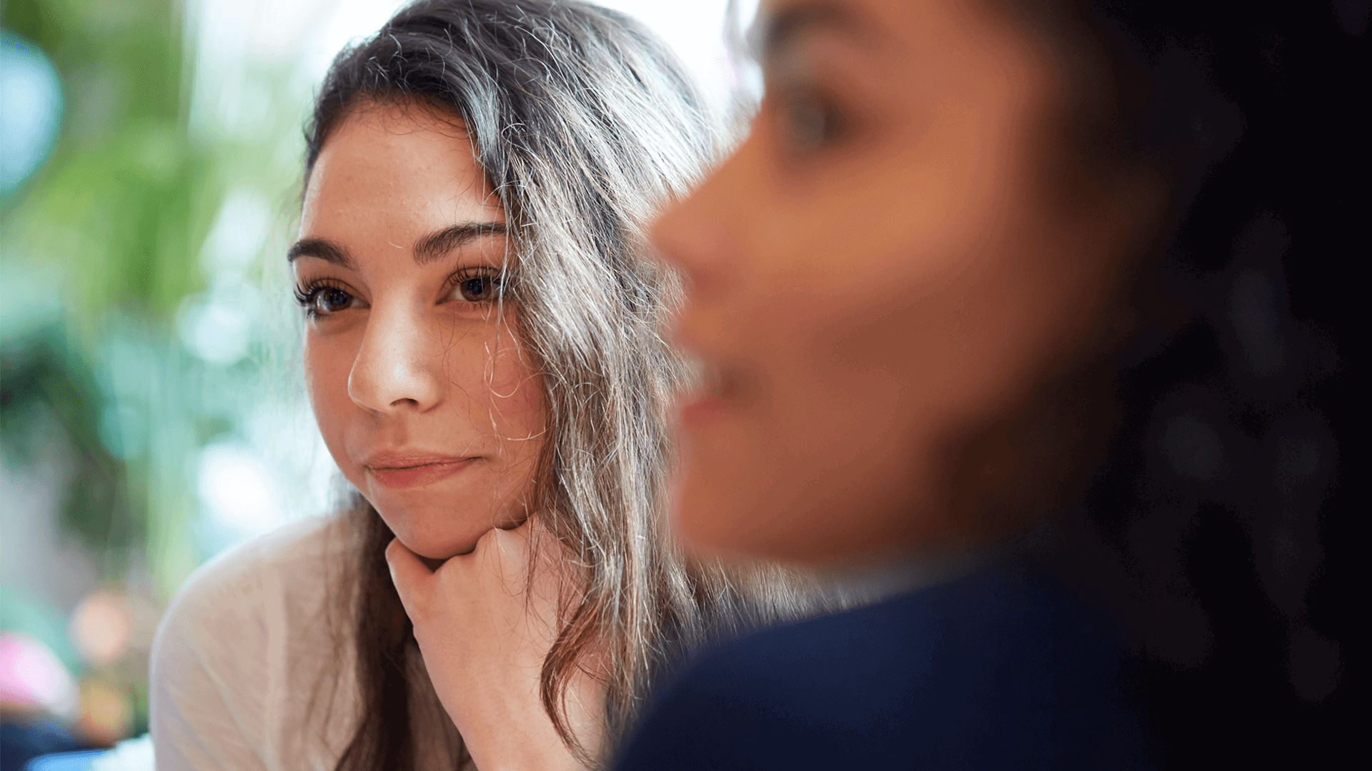 close up of a girl with long hair and one hand on chin listening to a person in front of her