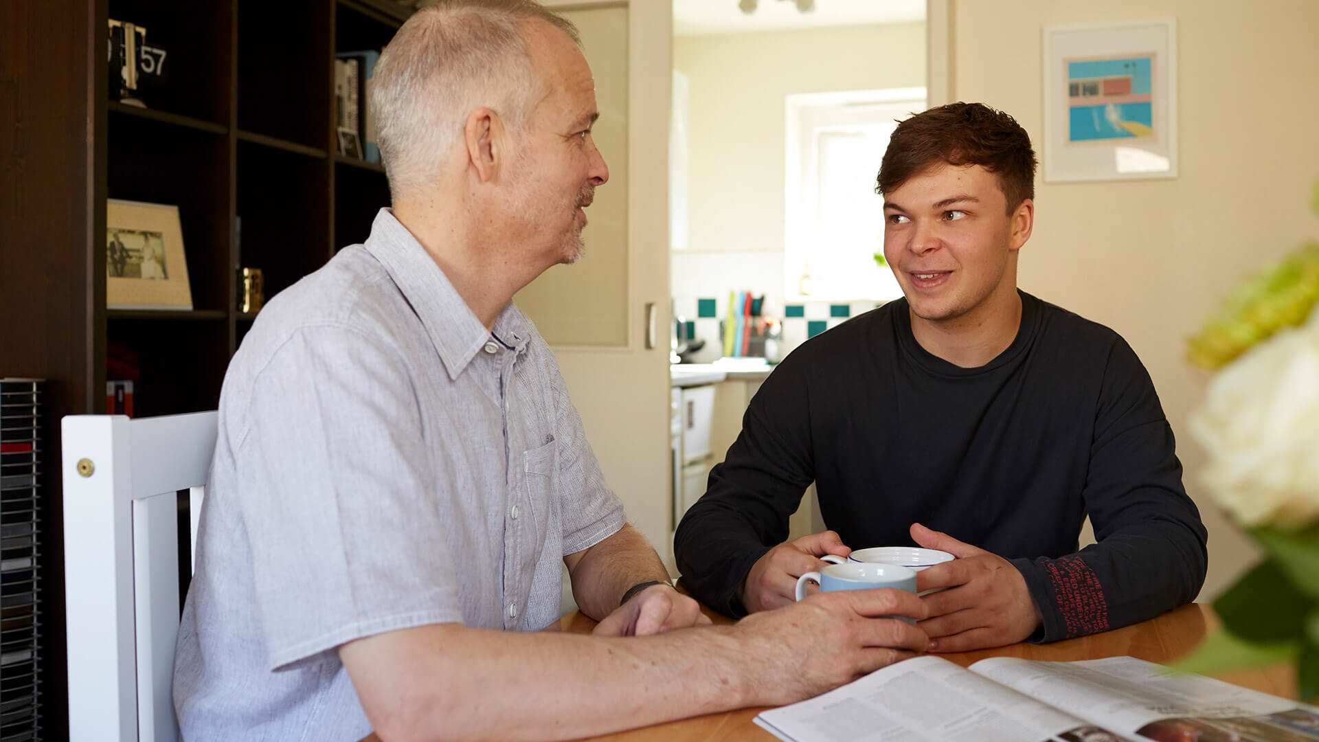 A father and son sitting at a table smiling with hot drinks