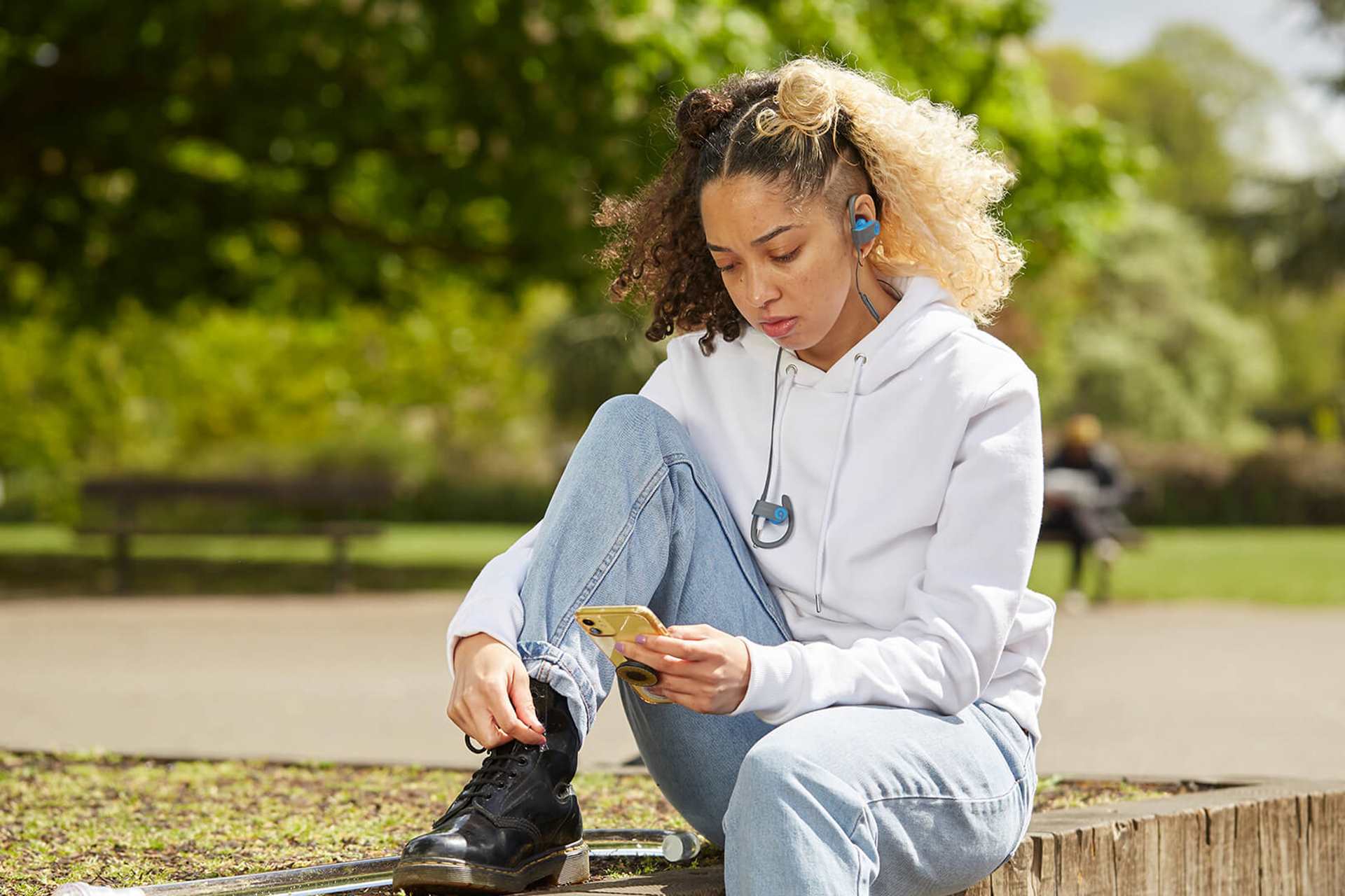 wide-shot-of-a-girl-with-headphones-and-looking-at-her-phones-while-sitting-in-the-park