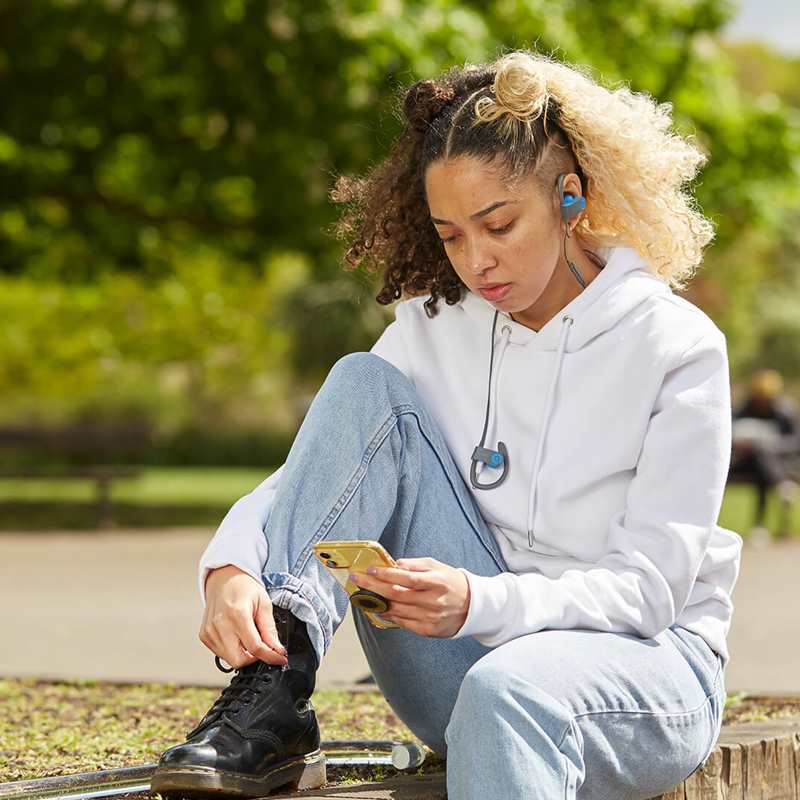 wide-shot-of-a-girl-with-headphones-and-looking-at-her-phones-while-sitting-in-the-park