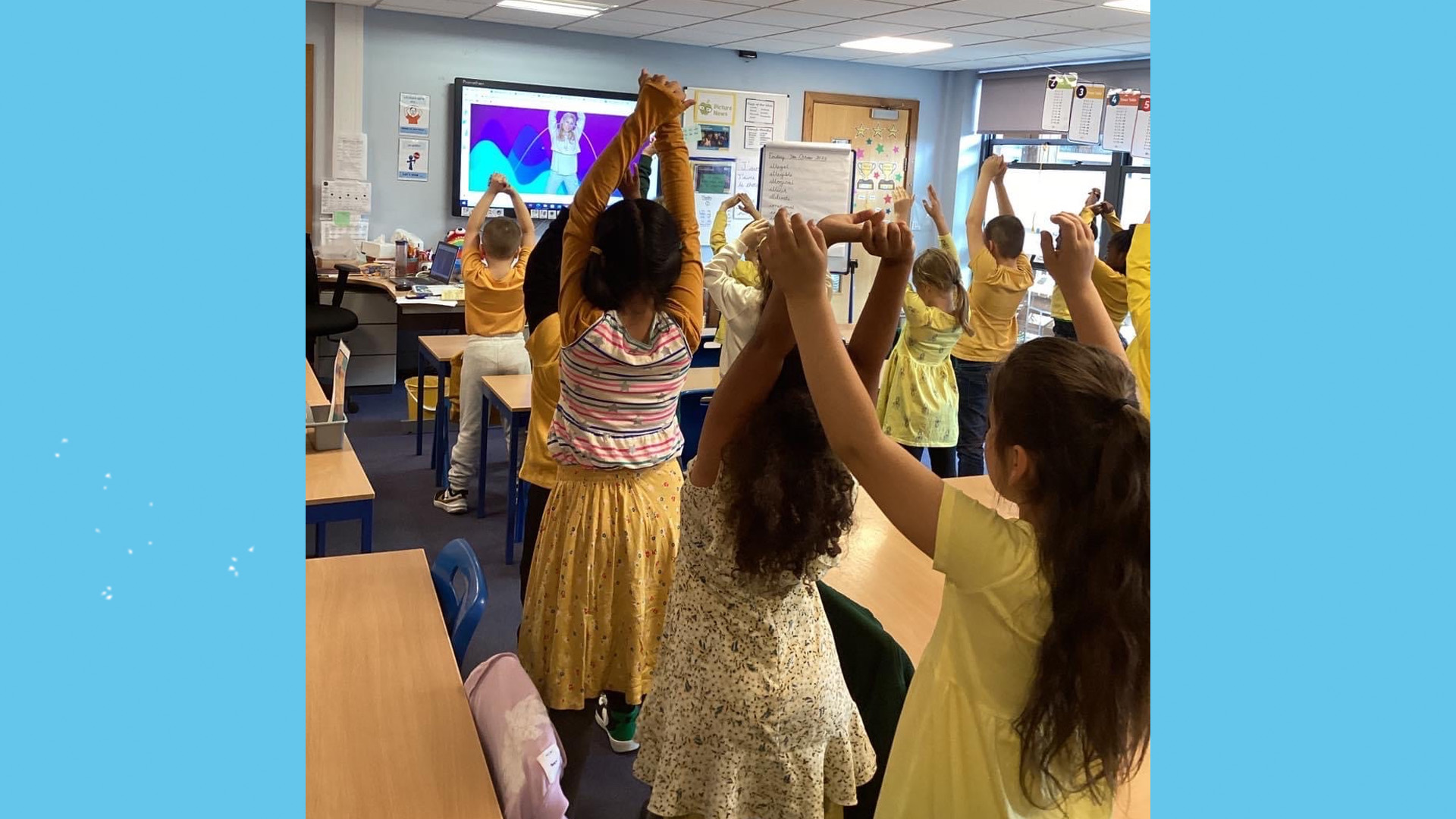 A primary school class all dressed in yellow with their hands in the air.