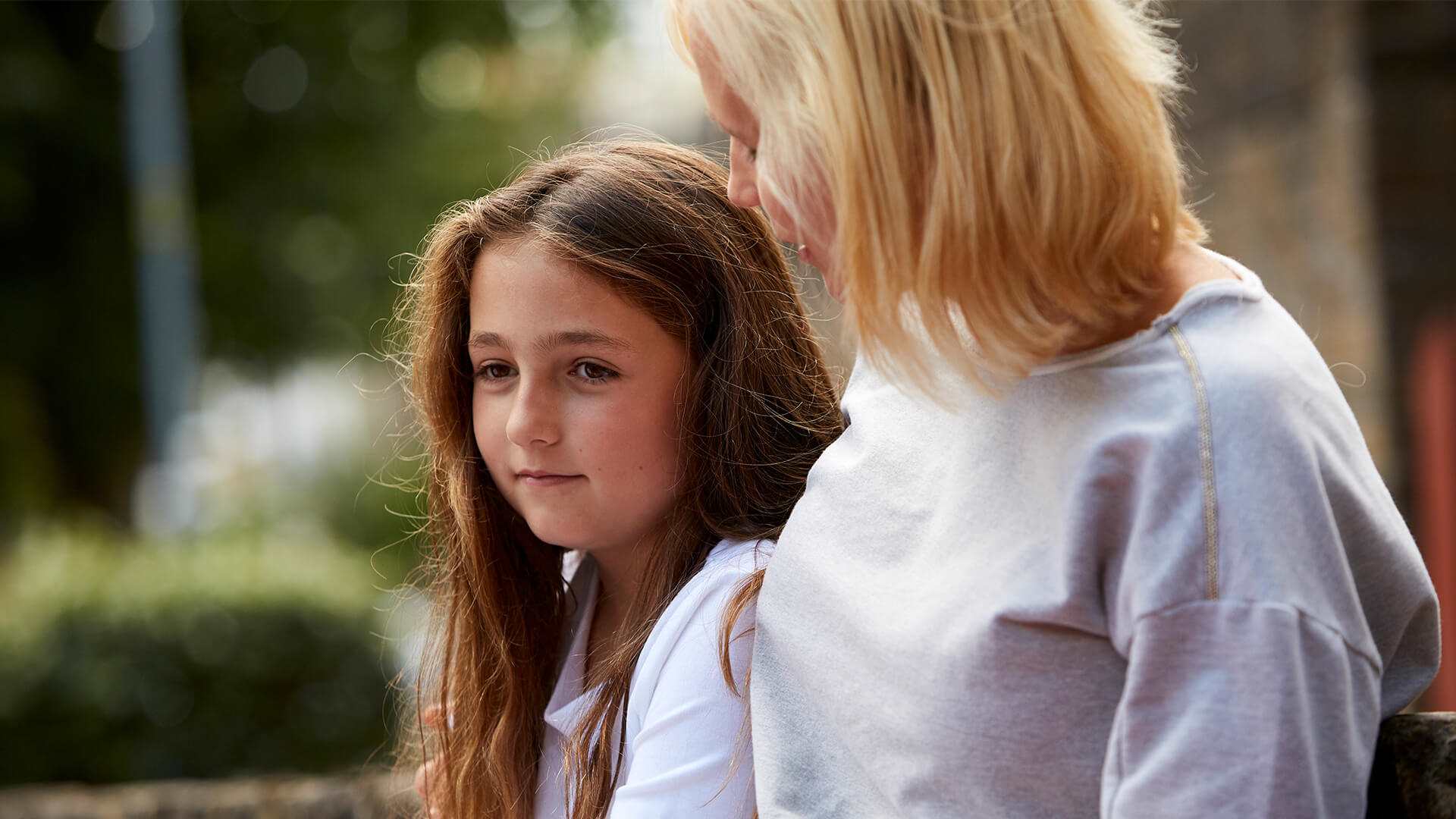 A mother comforts her sad looking daughter outdoors