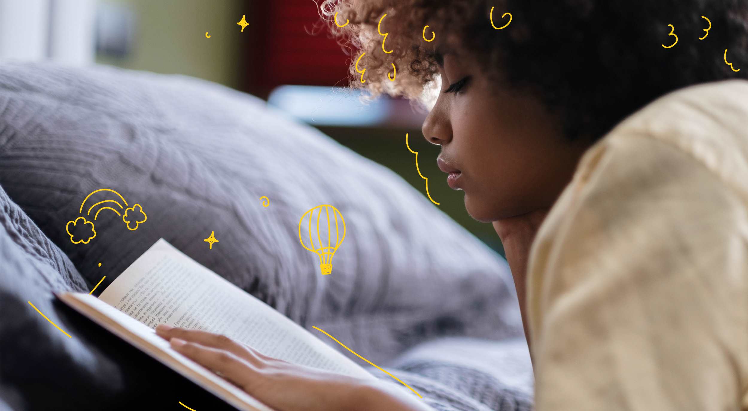 A young person reading a book lying on their front in bed.