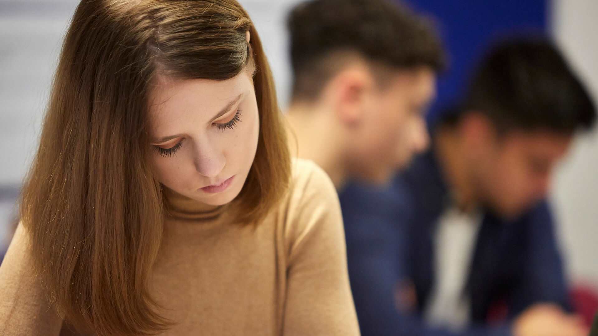 a-young-woman-in-brown-jumper-looking-down-with-sad-expression-with-two-young-men-blurred-on-the-background