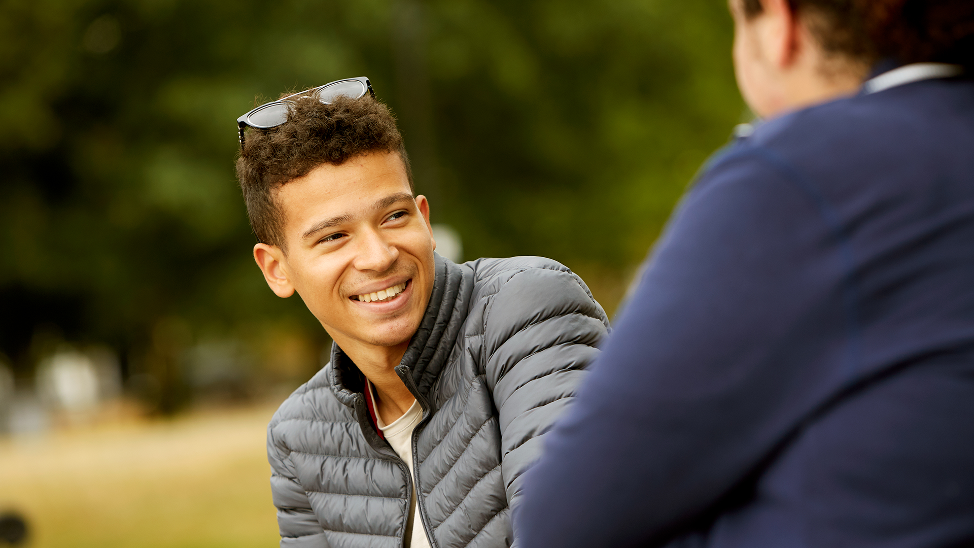 A boy smiling at his friend in the park.