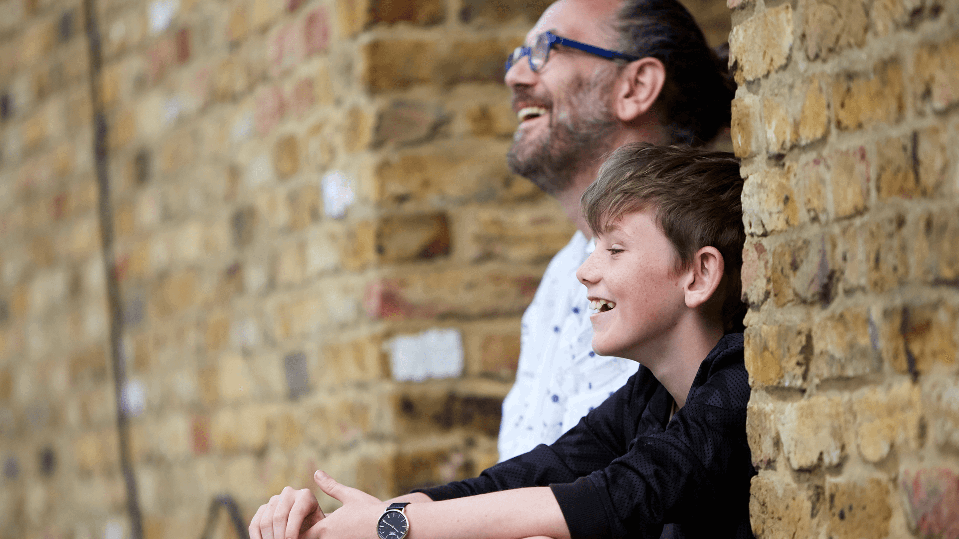 A father and son laughing and looking happy together by a wall