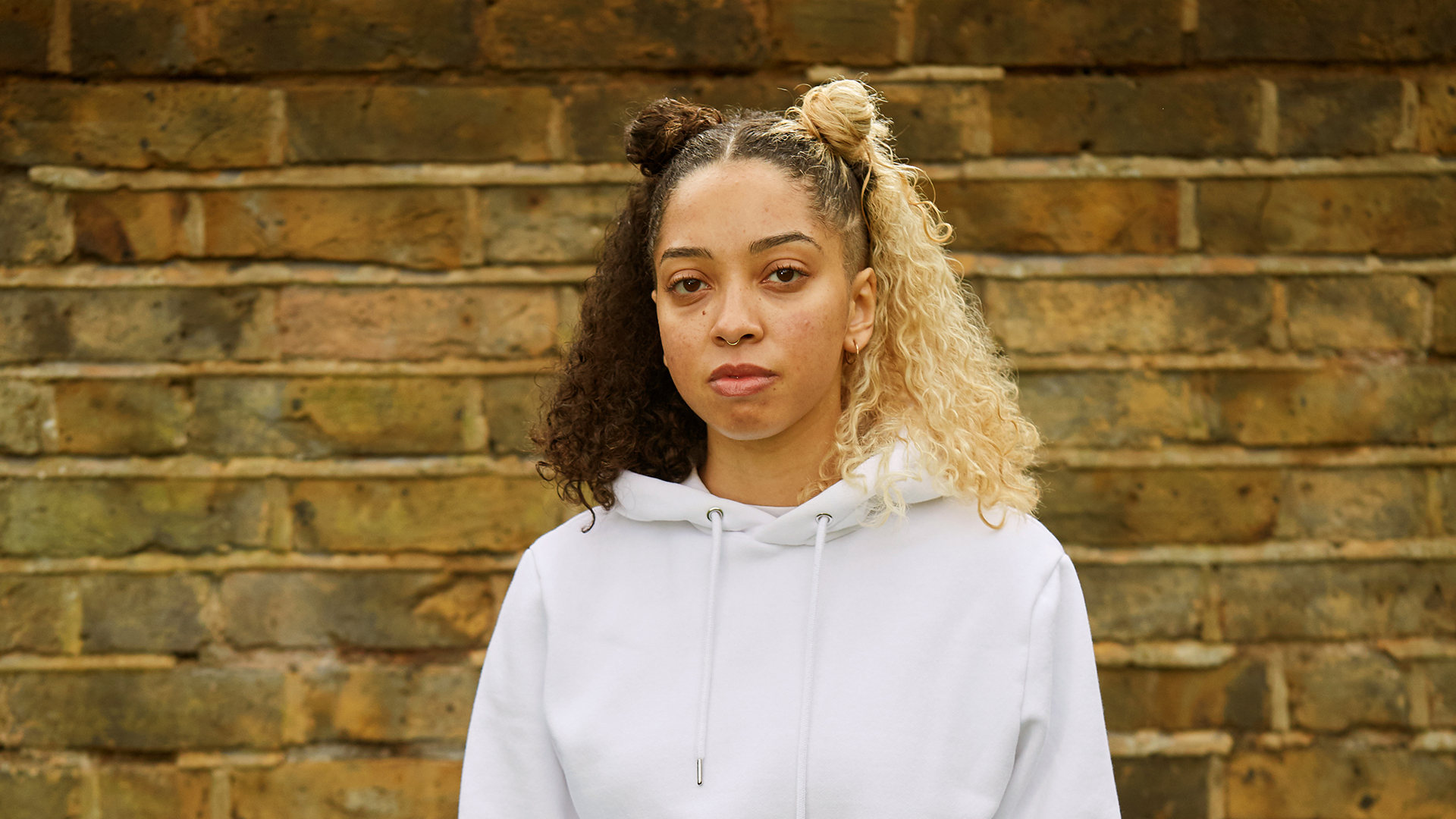 A girl staring at the camera in front of a brick wall.