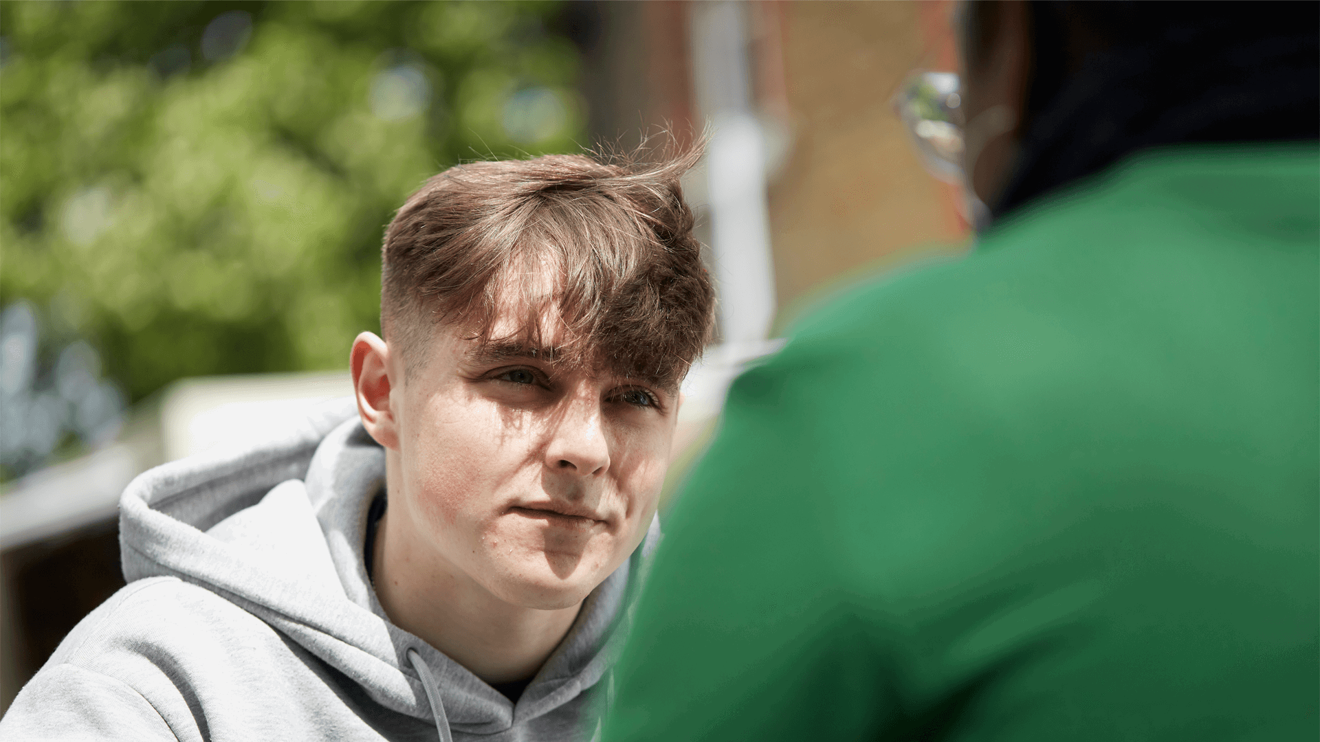 close up of a boy wearing grey hoodie listening to an advice of his teacher in front of him