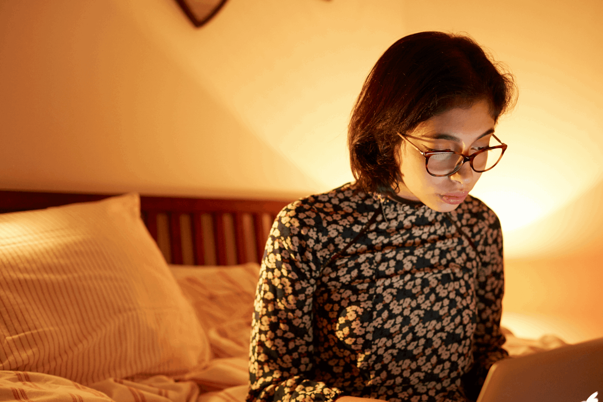 medium shot of a girl wearing glasses sitting on her bed while using her laptop