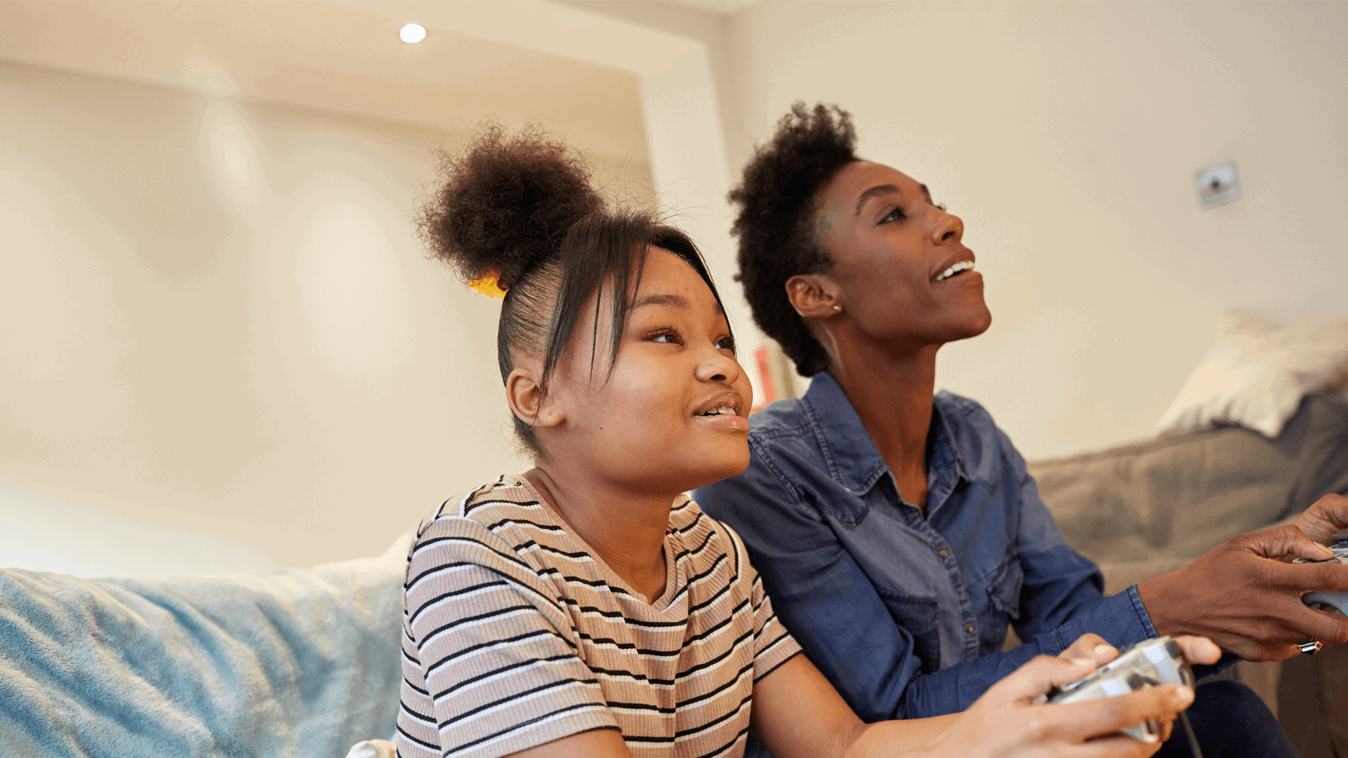 A mother and daughter playing video games together happily on the sofa